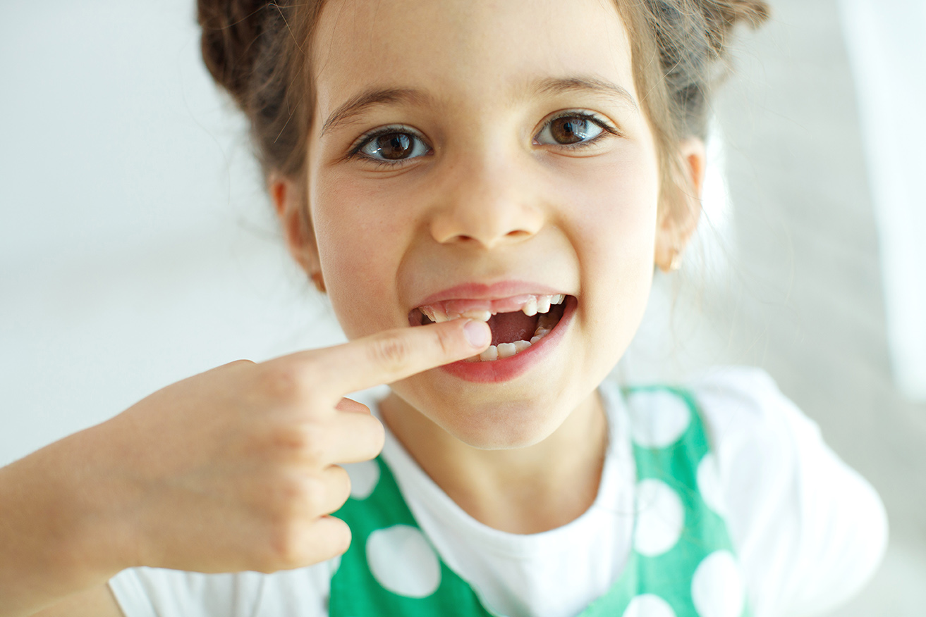 young girl pointing to her front tooth during a pediatric dental exam at timber ridge dental center